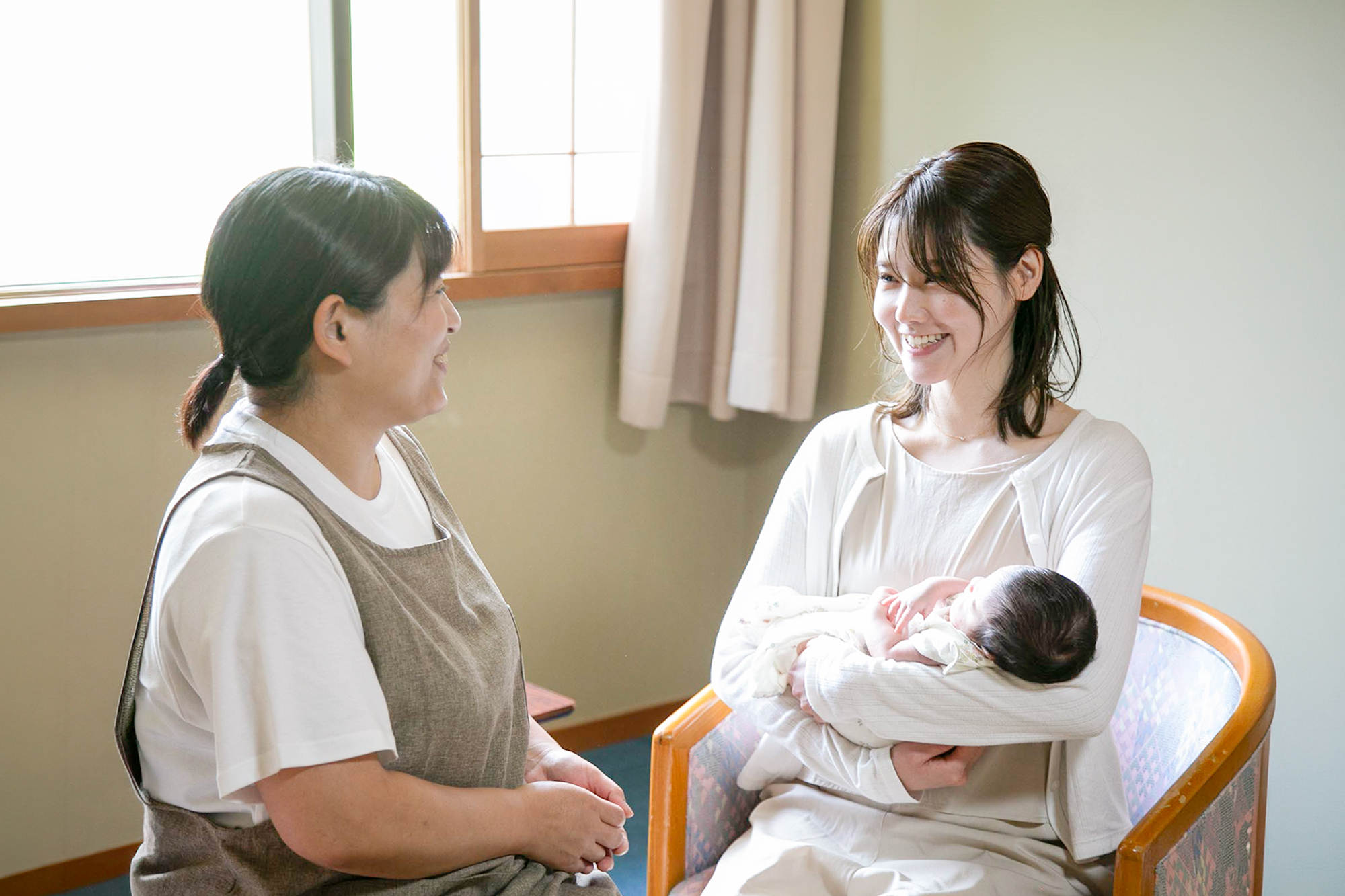 赤ちゃんを抱く妊婦さんに寄り添う看護師